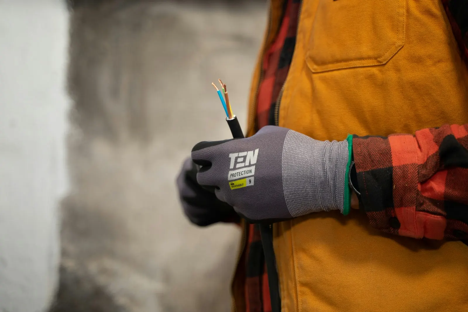 Elektriker in Arbeitsjacke hält mit Schutzhandschuh ein abisoliertes Kabel